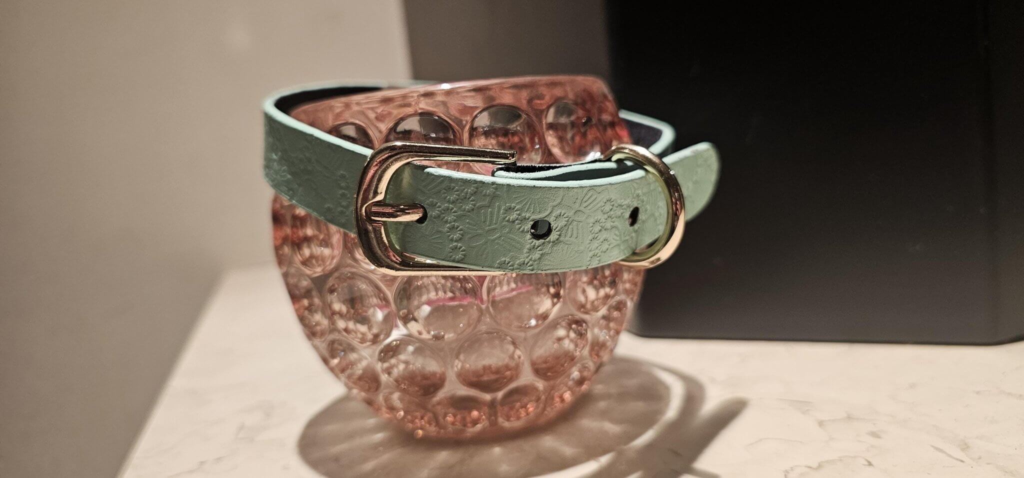 Elegant pastel blue leather collar on a decorative glass, ideal for submissive jewelry and BDSM aesthetics.