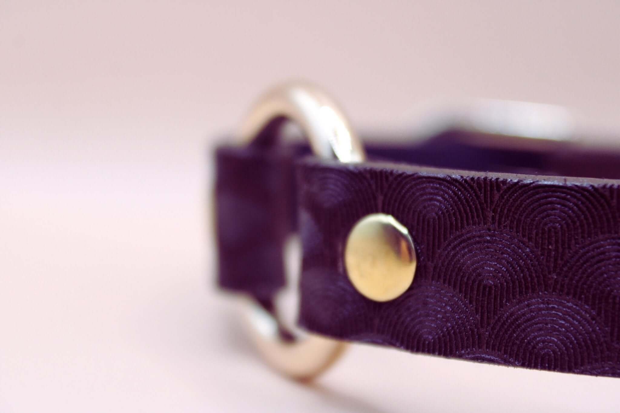 Close-up of elegant purple leather choker with scallop texture and gold hardware, perfect for BDSM and submissive jewelry.