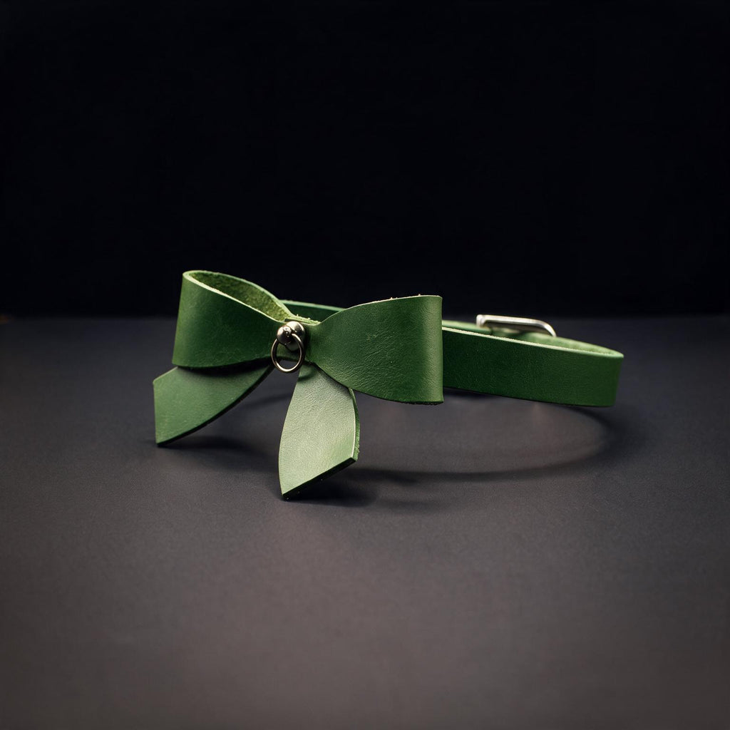 A green leather bow tie with a metal clasp is displayed against a dark background.