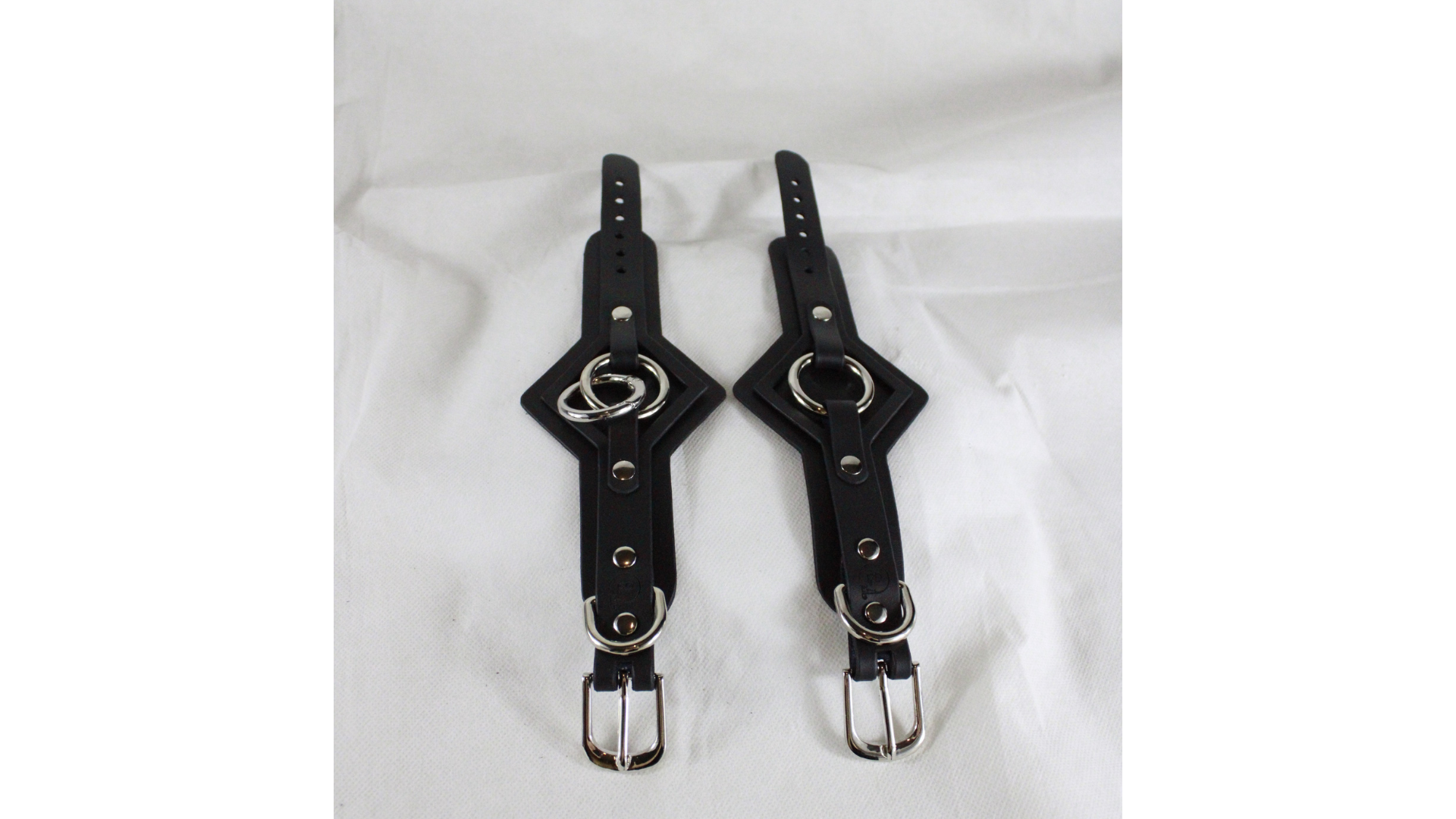 a pair of black leather straps with metal rings and buckles, placed side by side on a white background.