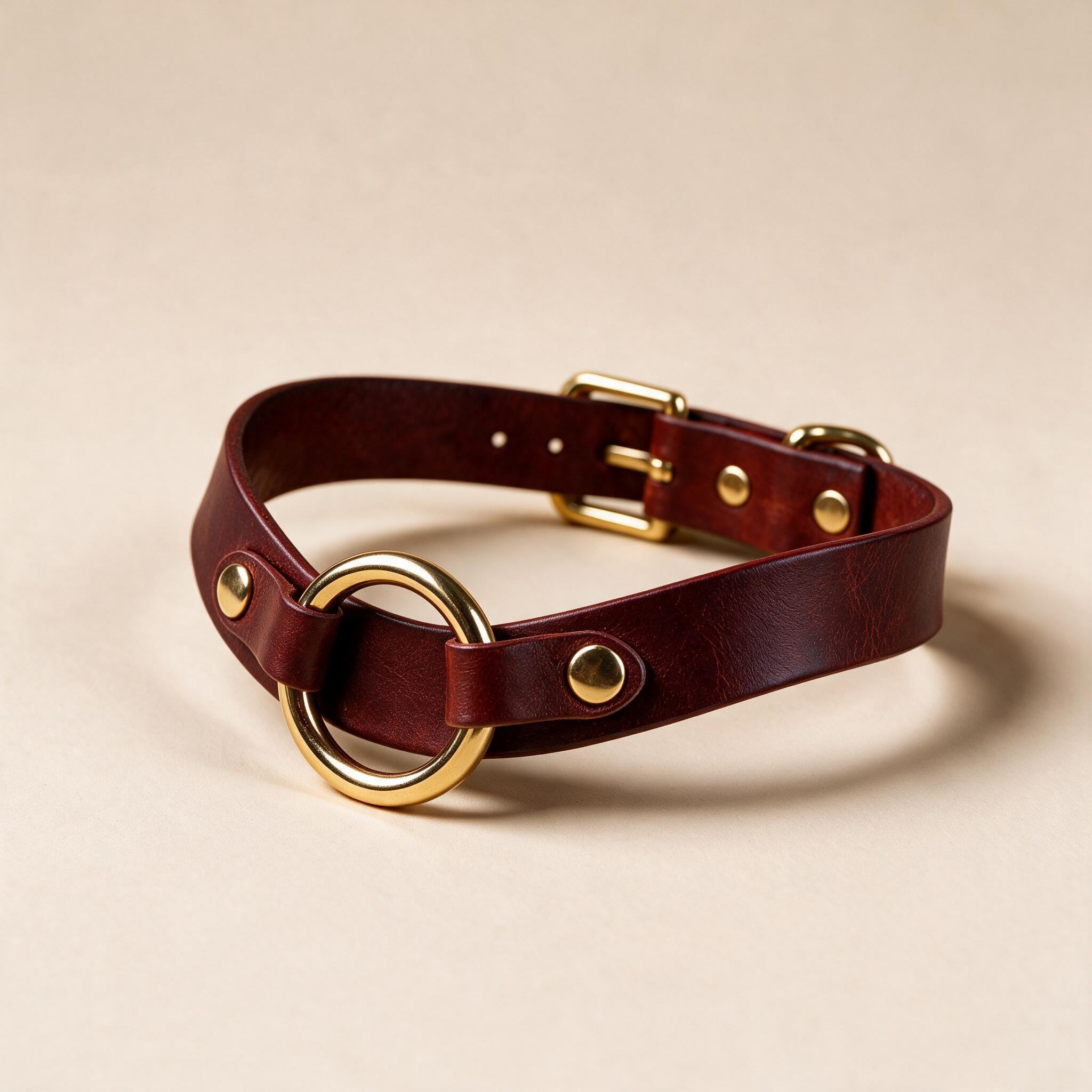 A burgundy leather choker collar with a gold-colored buckle and ring.