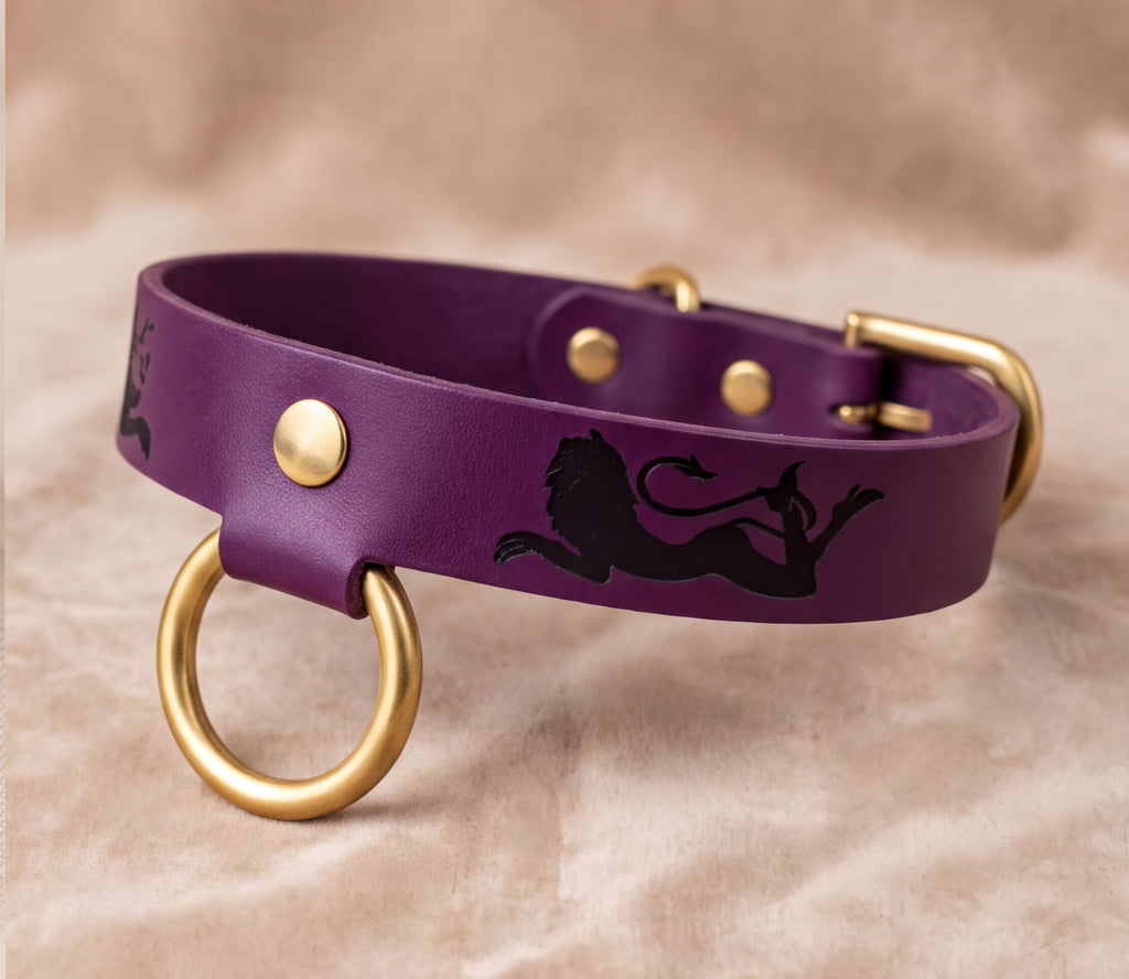 A purple leather dog collar with a lion design and gold-colored metal rings.