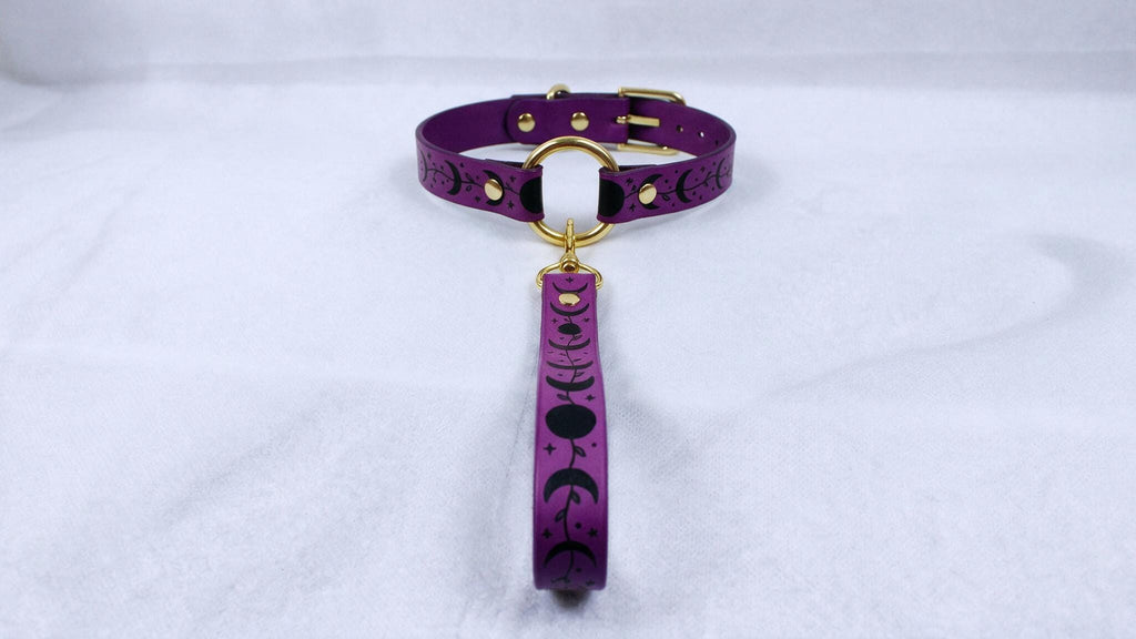 A purple collar with a gold buckle and a black and white design on it, placed on a white surface.