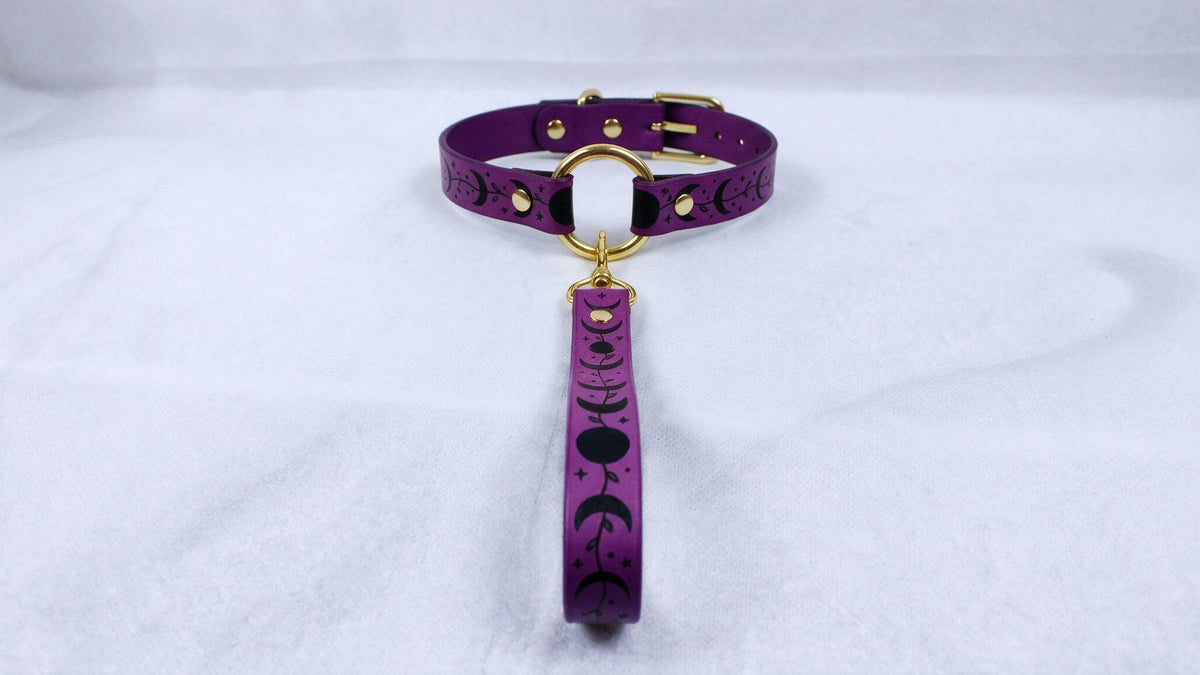 A purple collar with a gold buckle and a black and white design on it, placed on a white surface.