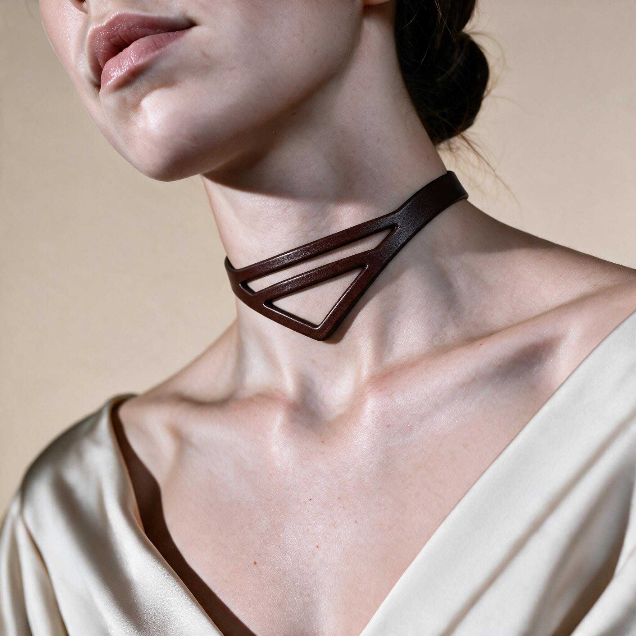 A close-up of a woman's neck and chest area, featuring a dark brown choker necklace with a triangular pendant.