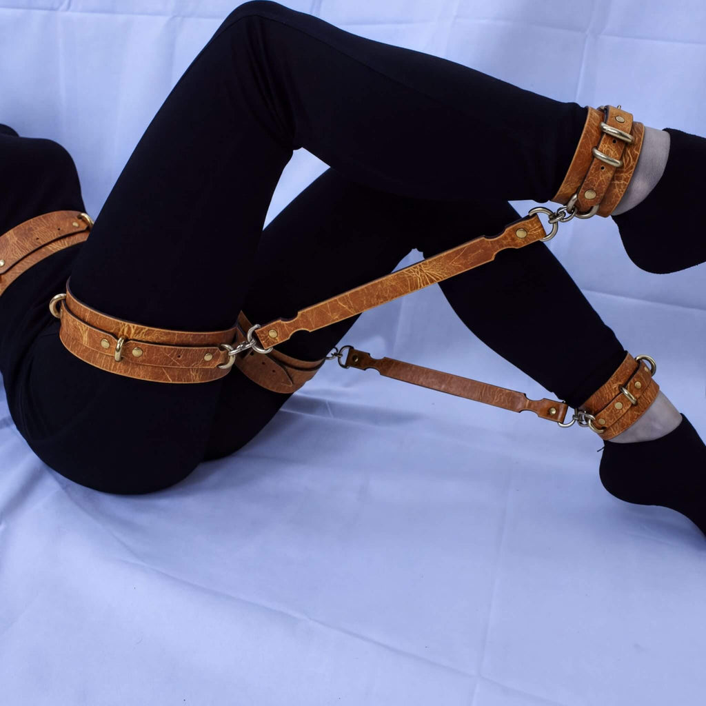 A person wearing black pants and leather straps on their legs, with their feet resting on a white surface.