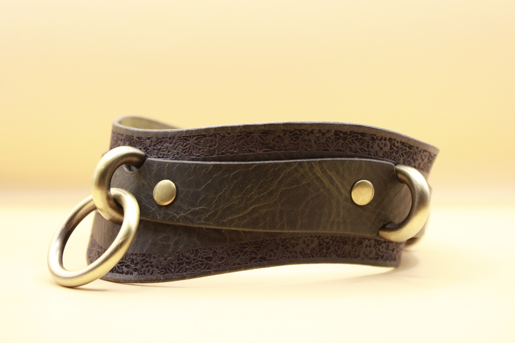 A brown leather choker necklace with metal rings and a decorative pattern on the edges.