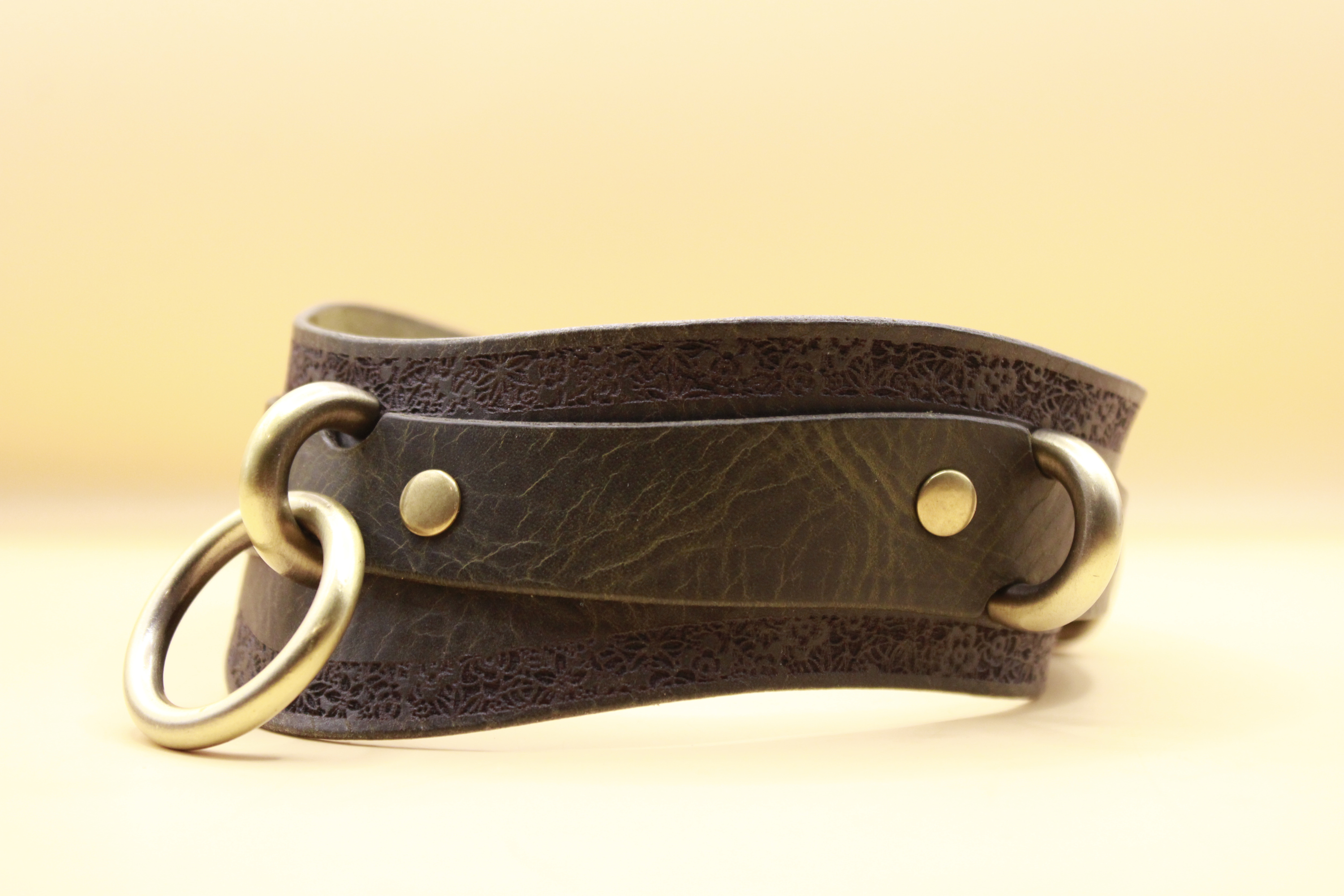 A brown leather choker necklace with metal rings and a decorative pattern on the edges.