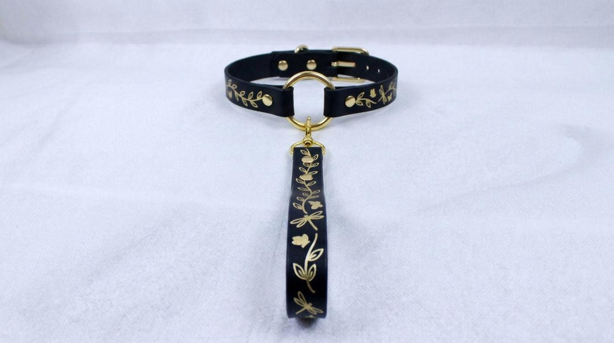 A black collar with gold leaf designs and a gold-colored tag hanging from it.