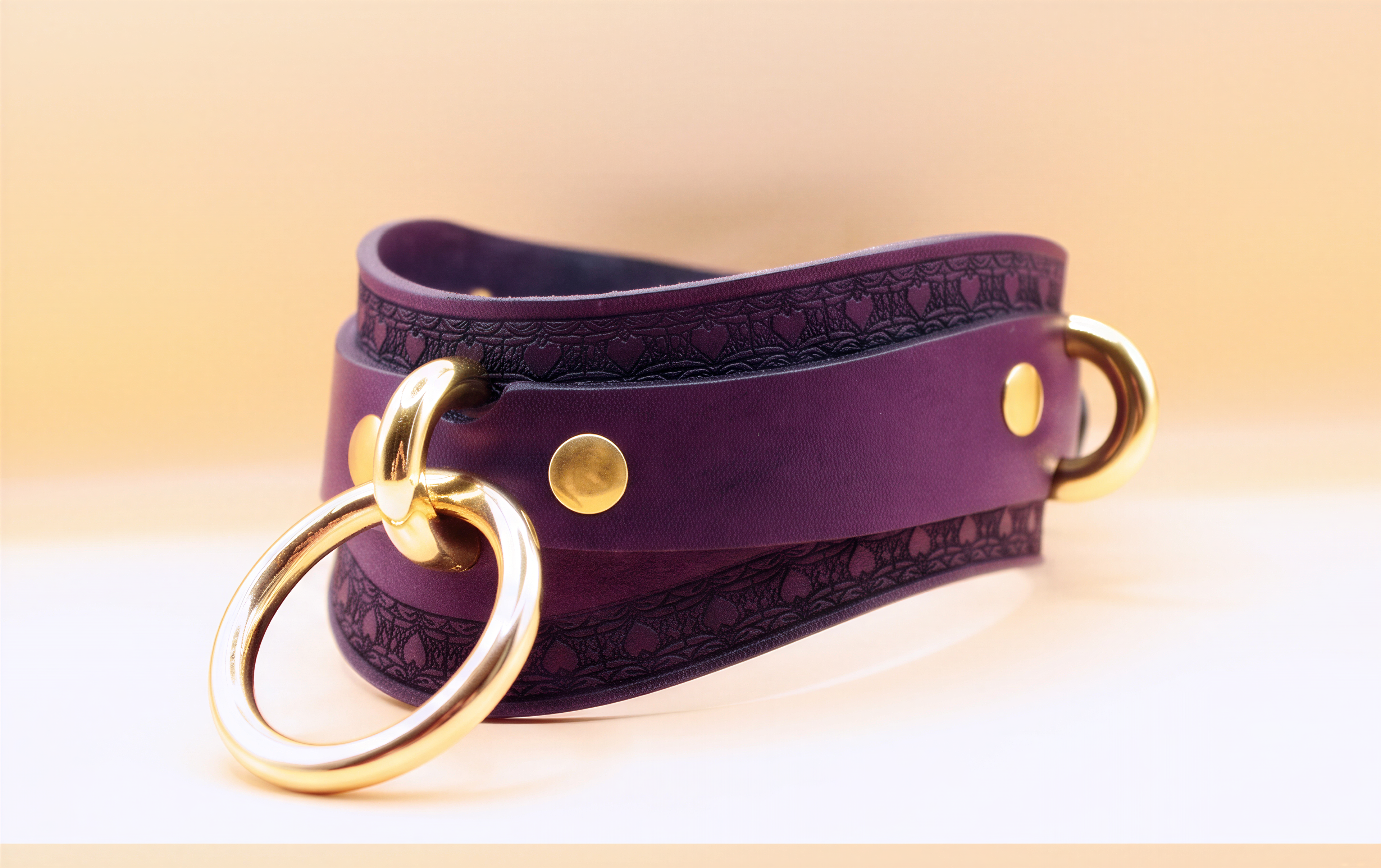A purple leather choker necklace with a gold ring and two gold-colored metal rings on either side.