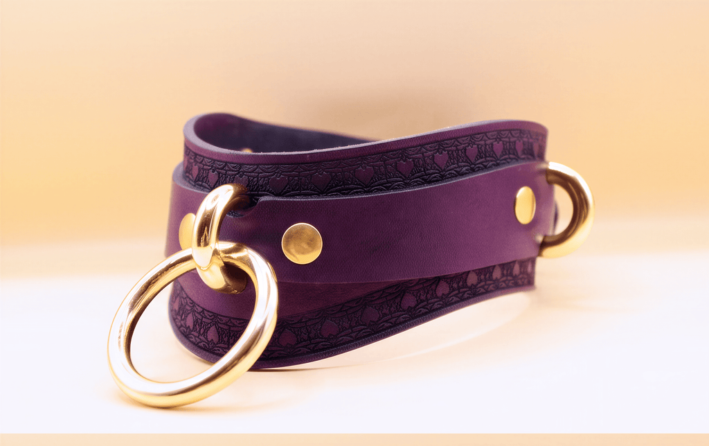 A purple leather choker necklace with a gold ring and two gold-colored metal rings on either side.