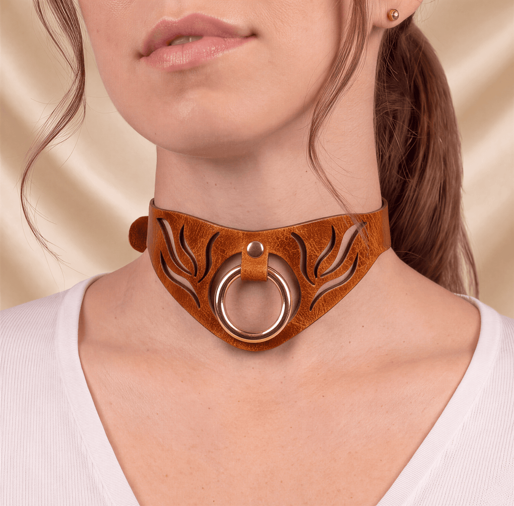 A close-up of a woman's neck and chest area wearing a brown leather choker necklace with a gold ring.