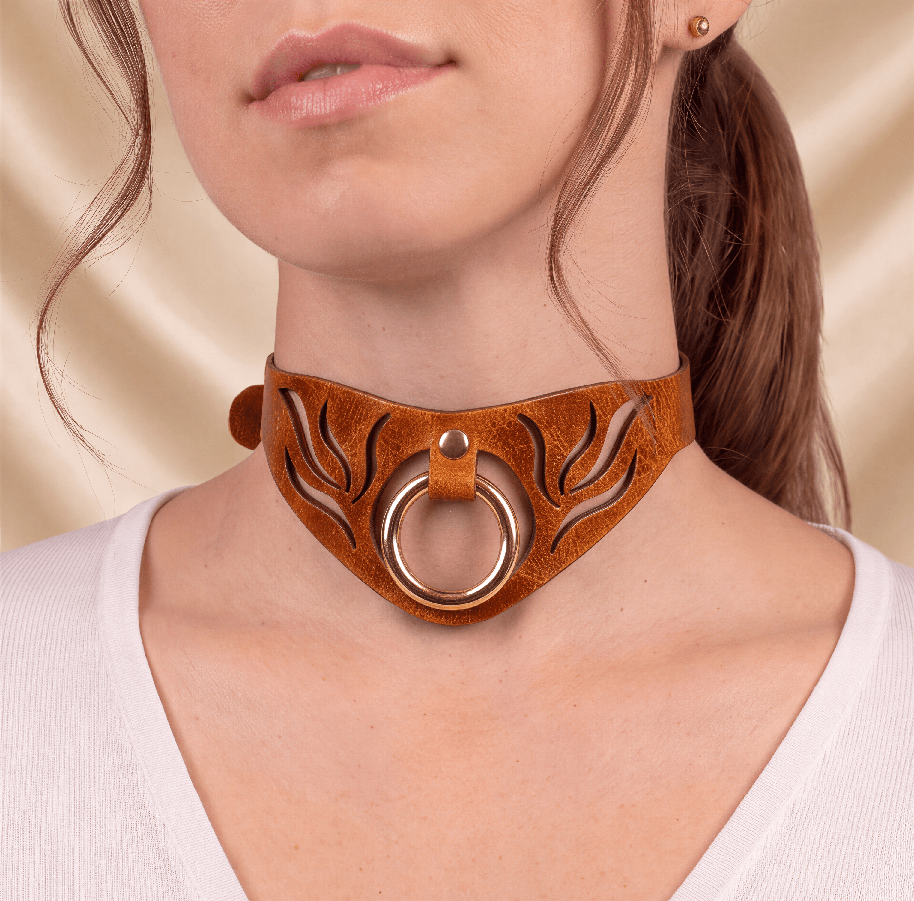 A close-up of a woman's neck and chest area wearing a brown leather choker necklace with a gold ring.