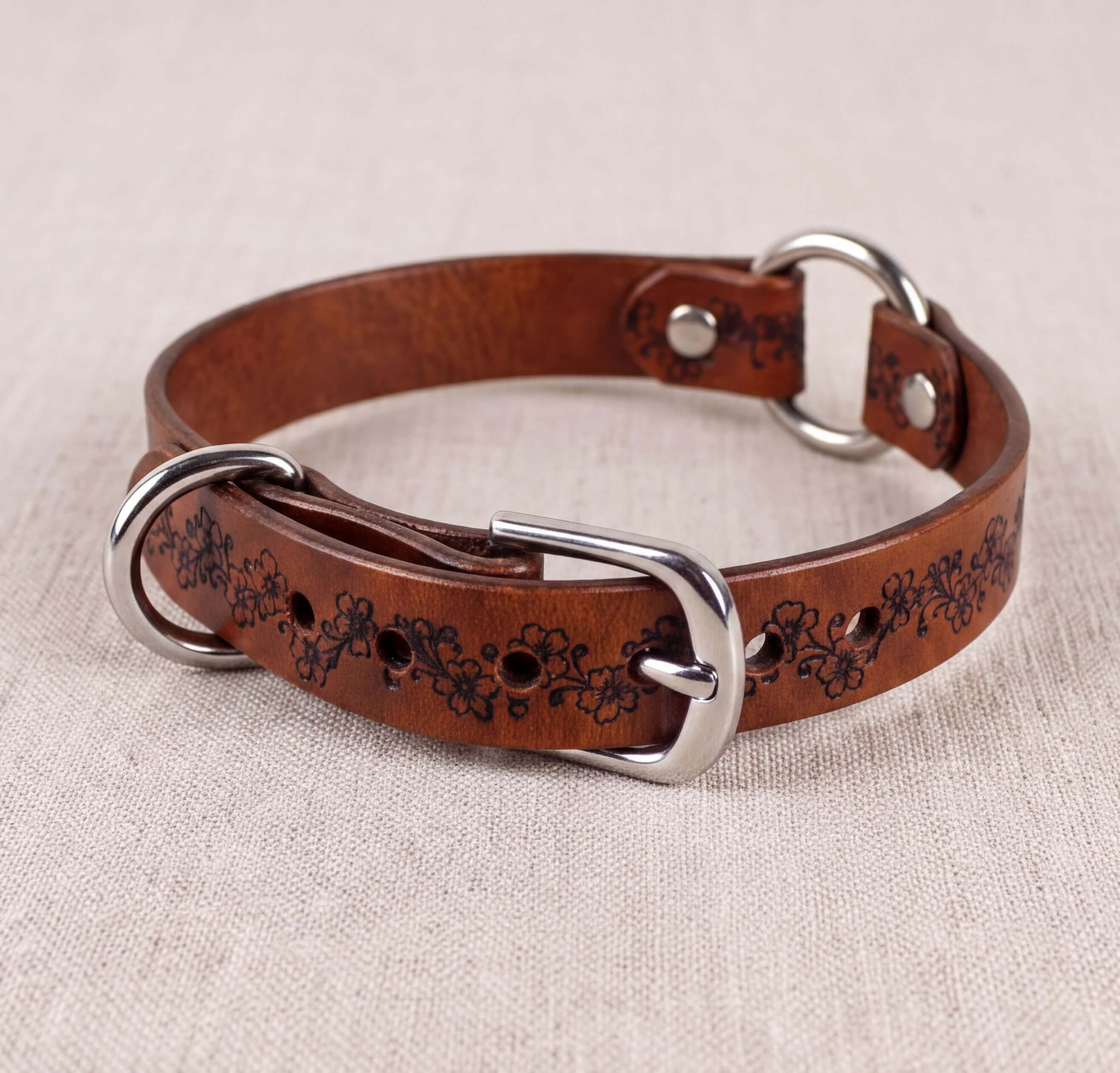 A brown leather dog collar with a floral pattern and metal buckle.