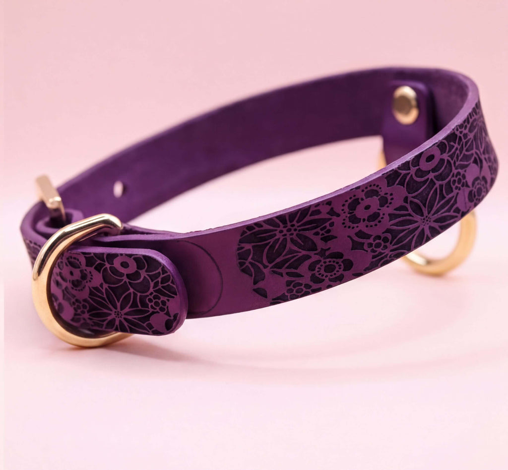 A purple leather dog collar with a floral pattern and a gold-colored buckle.