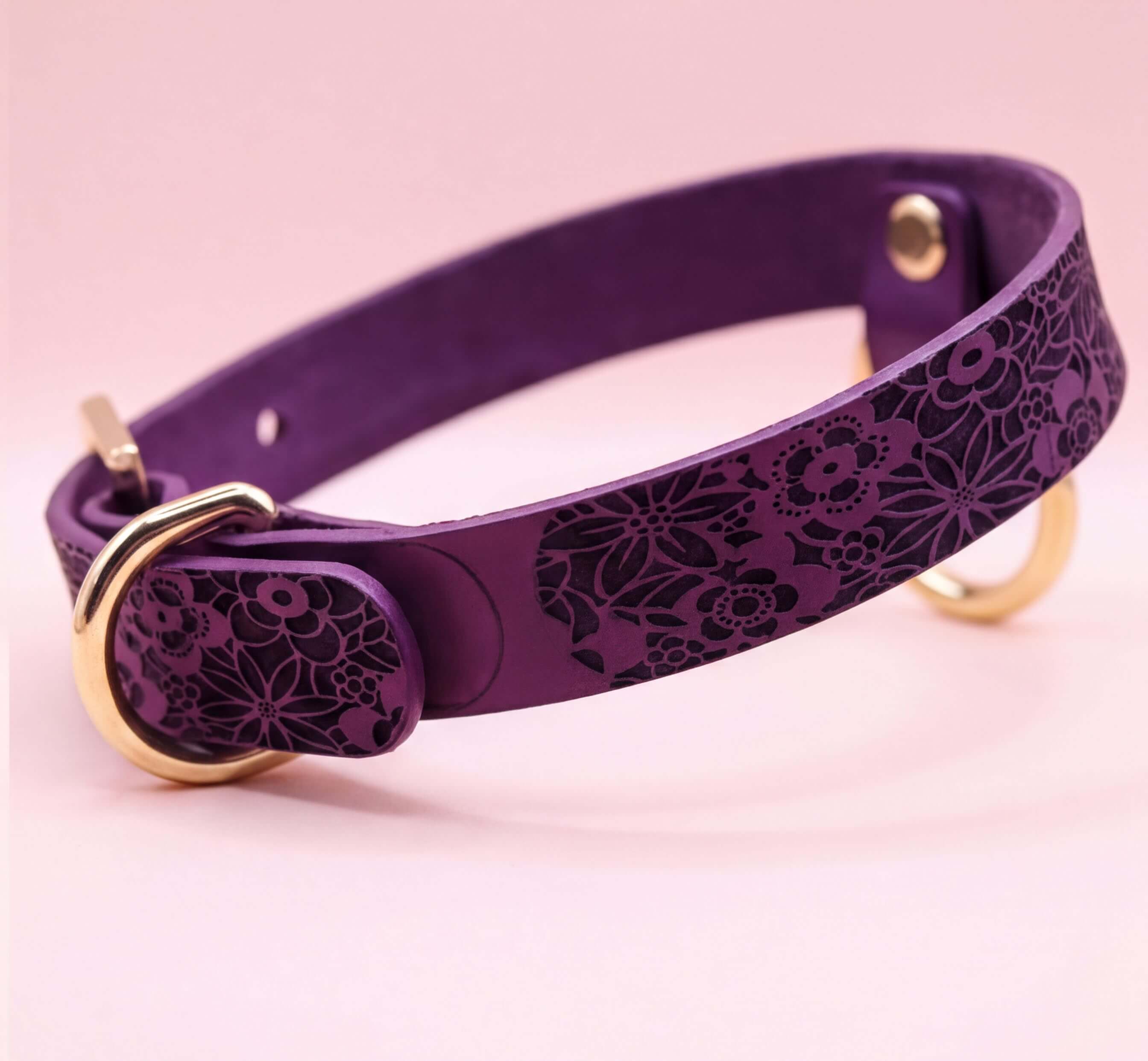 A purple leather dog collar with a floral pattern and a gold-colored buckle.