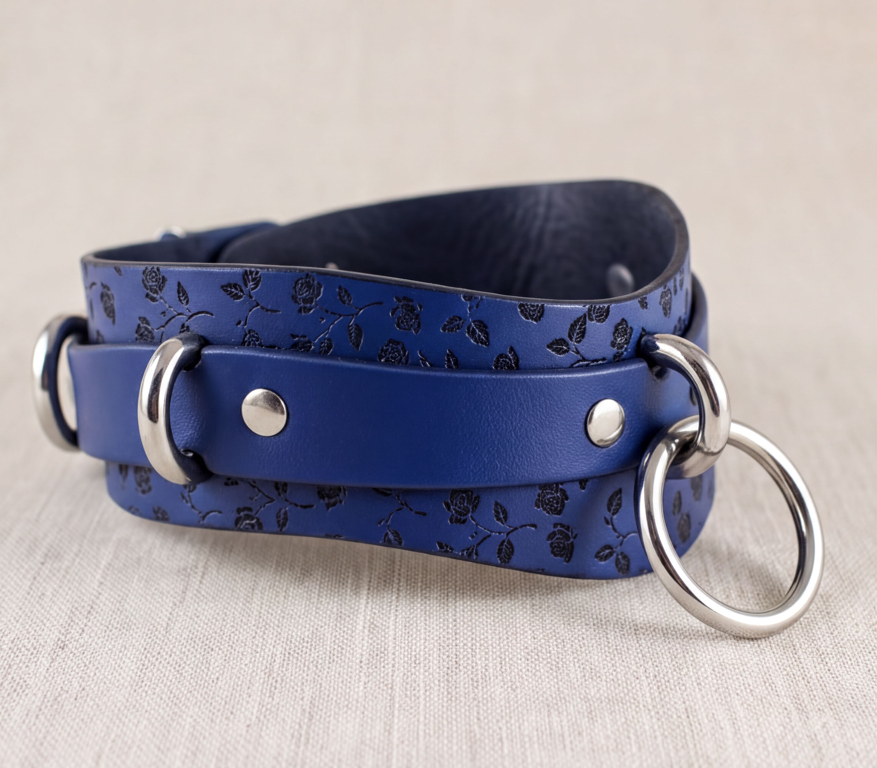 A blue leather strap with a floral pattern and metal rings on it.