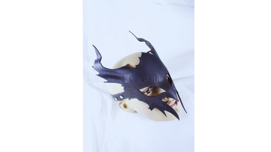 A dark, ornate mask with a pointed design and sharp edges is displayed against a plain white background.
