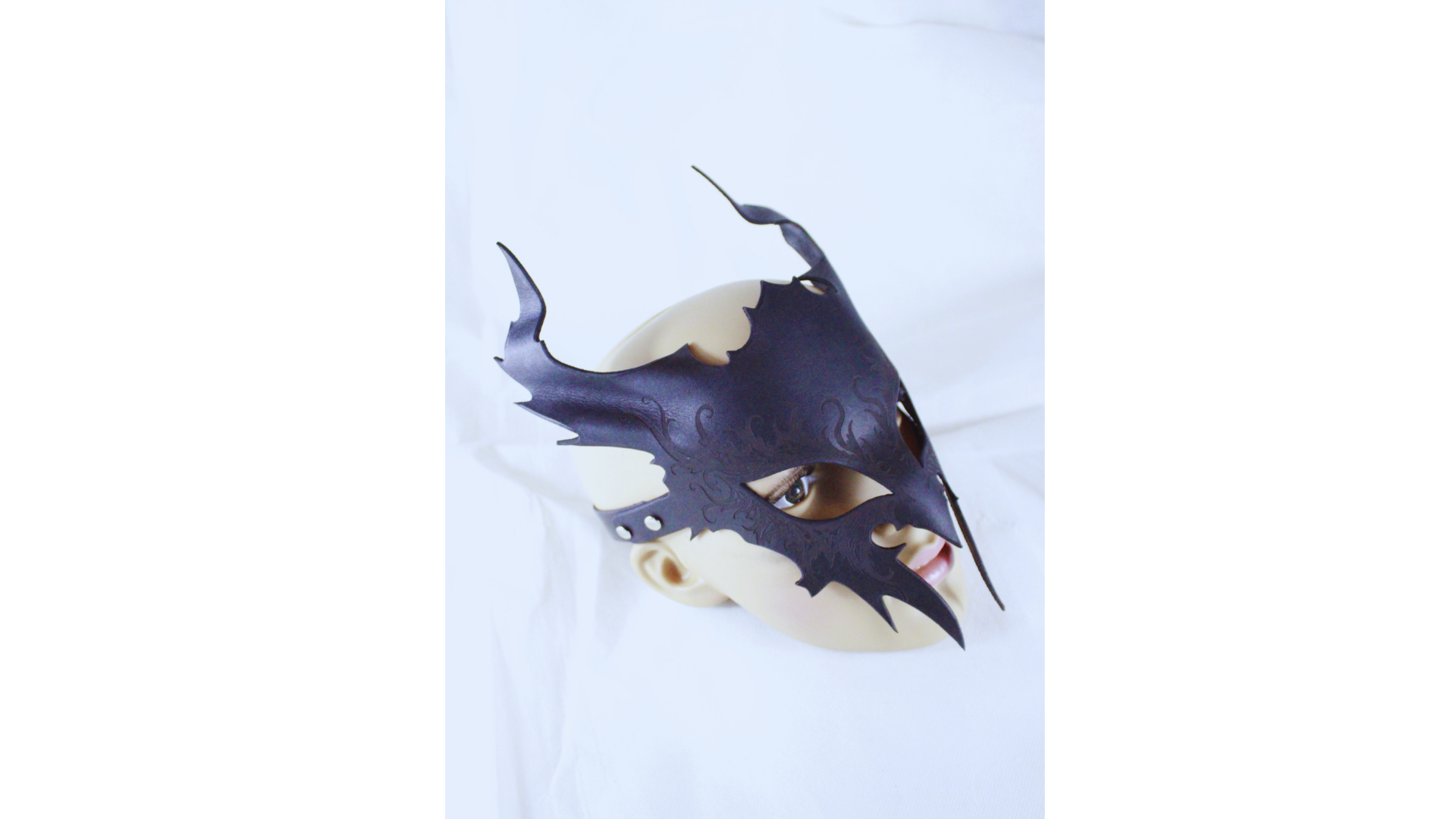 A dark, ornate mask with a pointed design and sharp edges is displayed against a plain white background.