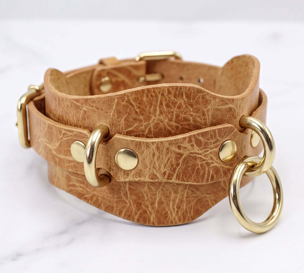 A tan leather choker necklace with gold-colored metal rings and buckles.