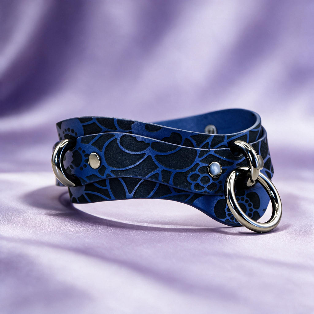 A blue leather choker necklace with a floral pattern and metal rings on the ends, resting on a purple background.