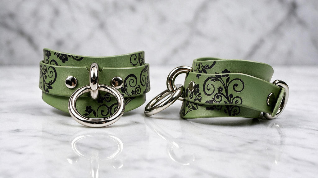 A pair of green leather choker necklaces with black floral designs and metal rings on the front.