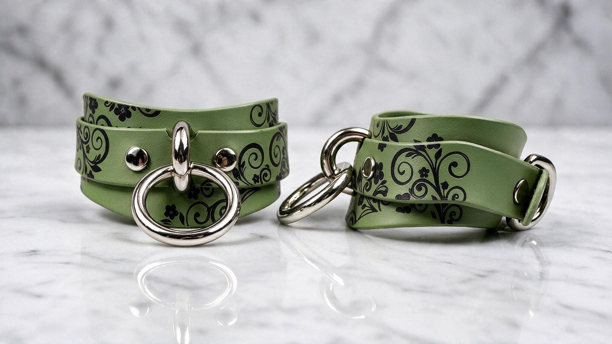 A pair of green leather choker necklaces with black floral designs and metal rings on the front.