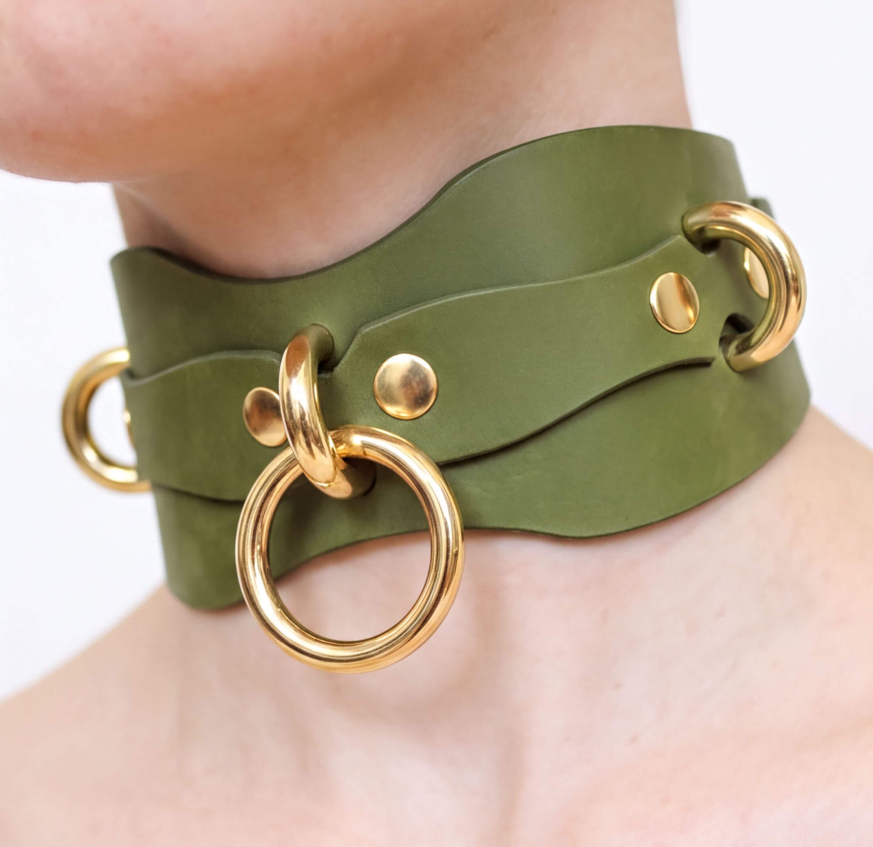 A close-up of a person's neck wearing a green leather choker necklace with gold-colored metal rings.