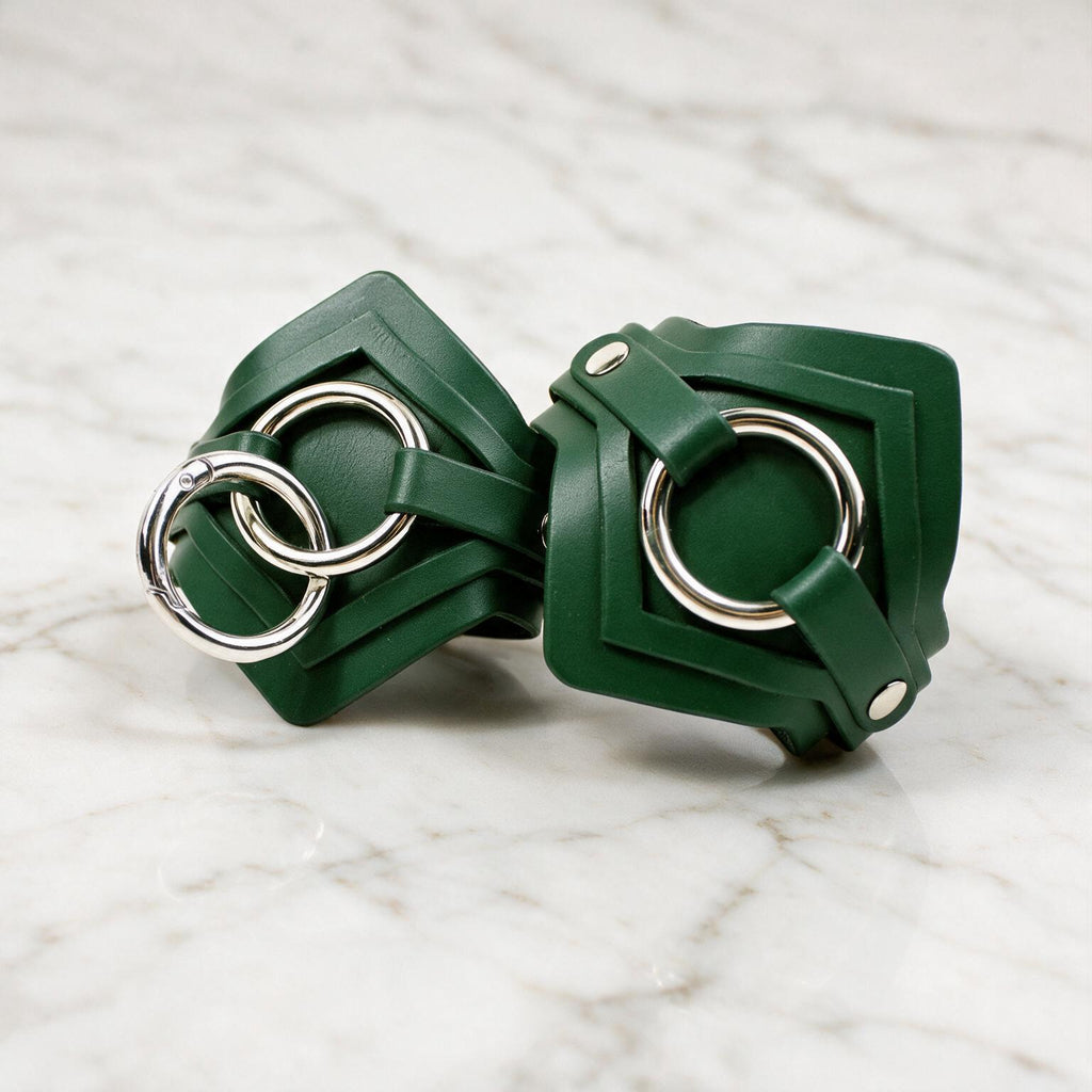 A pair of green leather cuffs with silver metal rings on them, placed on a marble surface.