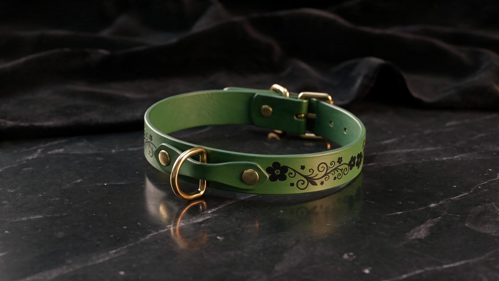 A green leather collar with a floral design and gold hardware is displayed on a black marble surface.