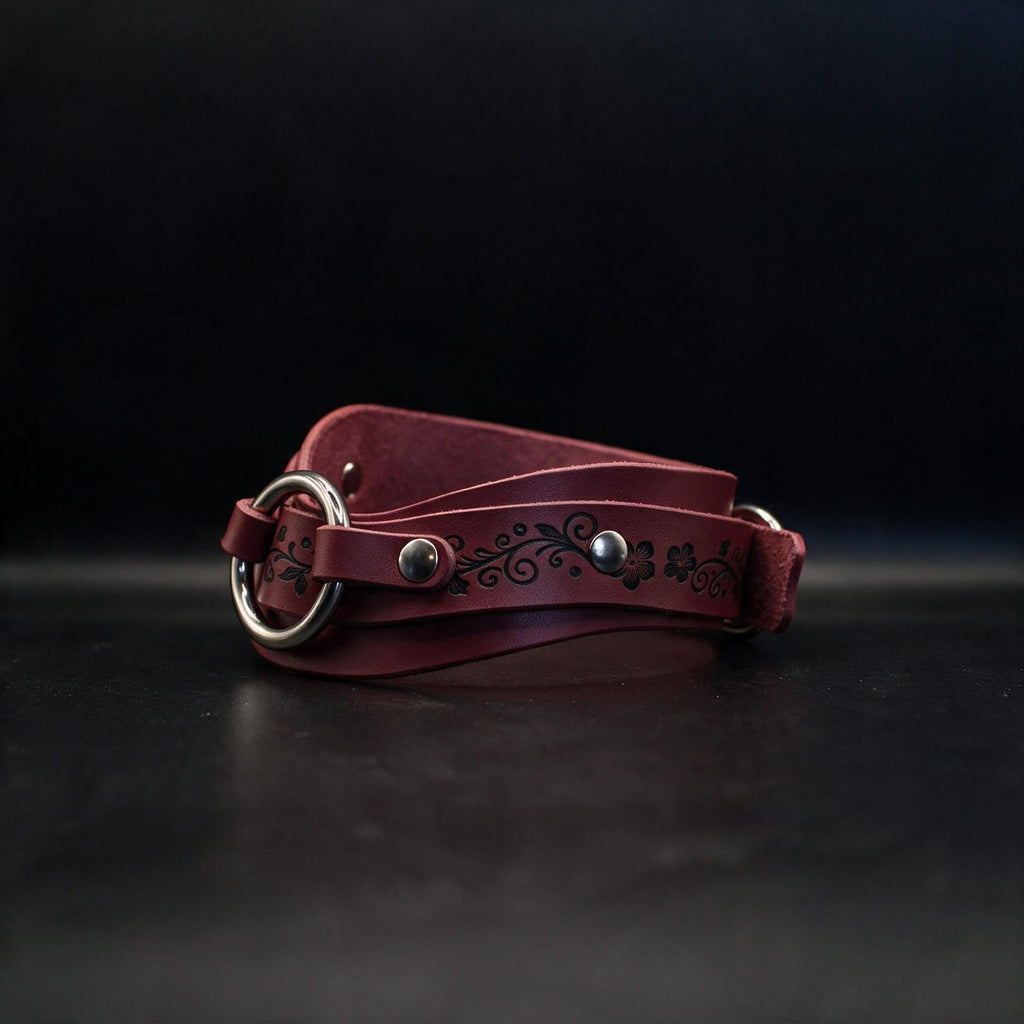 A burgundy leather belt with a floral design on the buckle is displayed against a black background.
