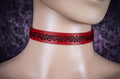 A red choker necklace with a black engraved design on the front.