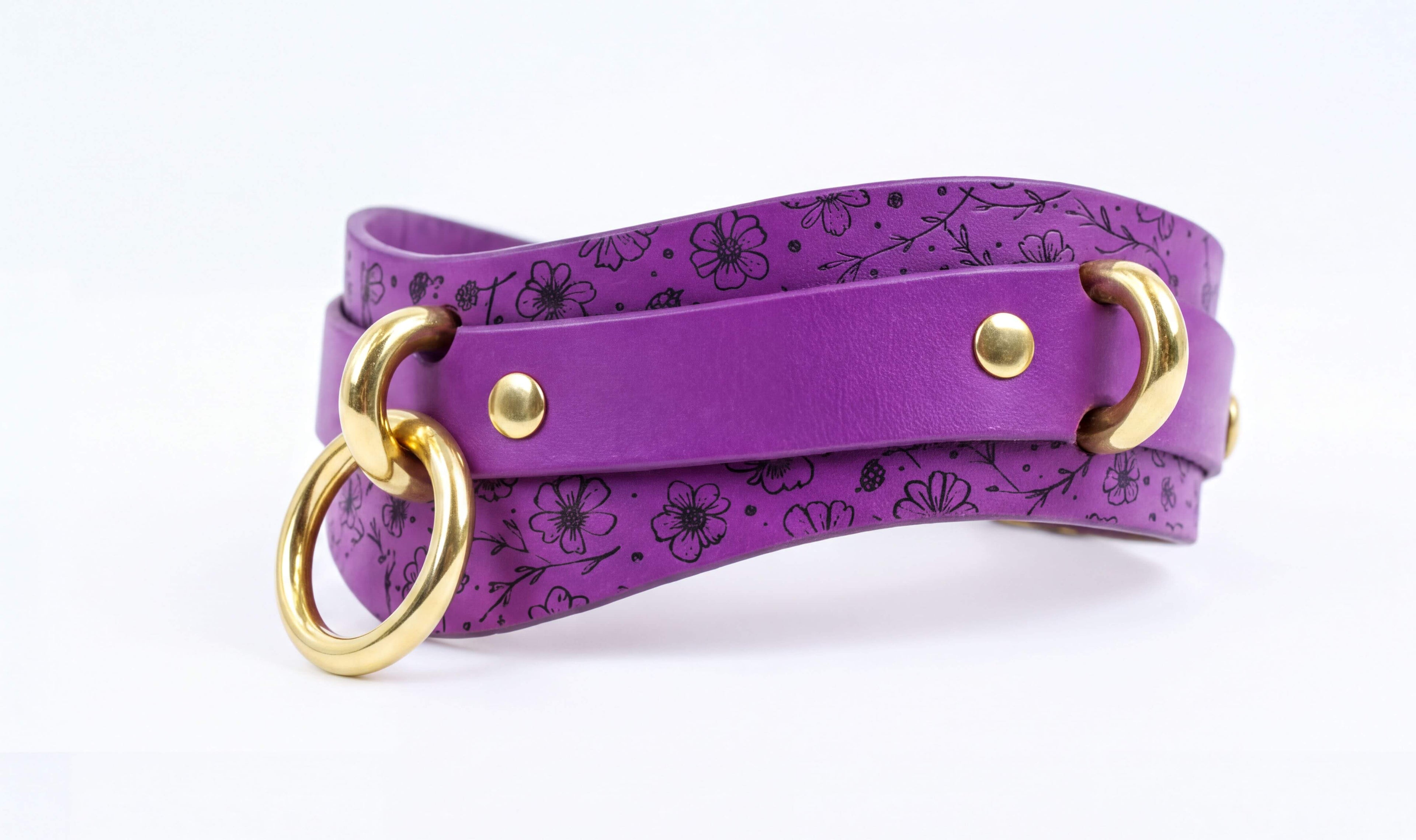 A purple leather choker necklace with a floral pattern and two gold-colored metal rings.