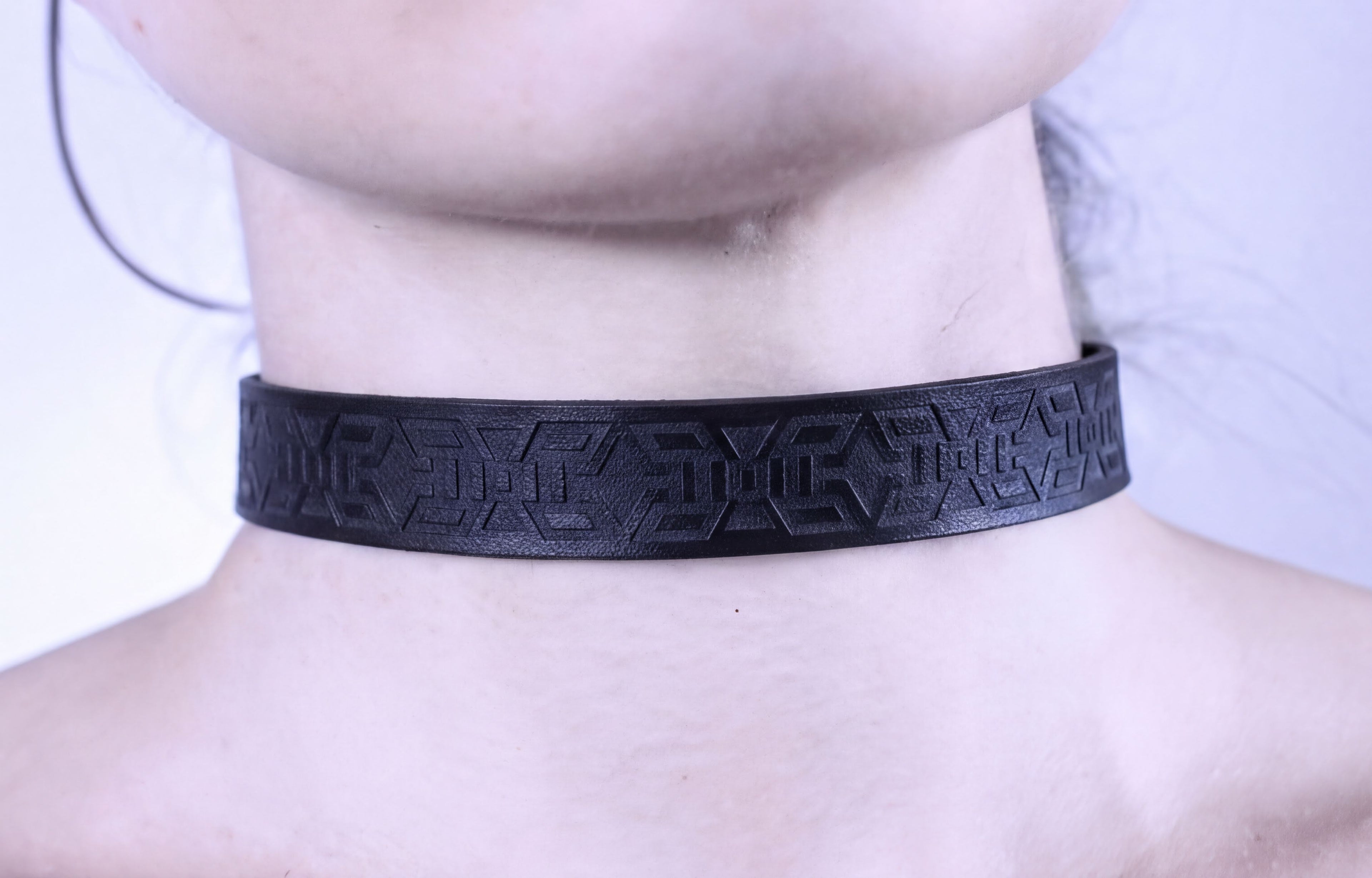 A close-up view of a person's neck wearing a black choker necklace with an intricate geometric pattern.