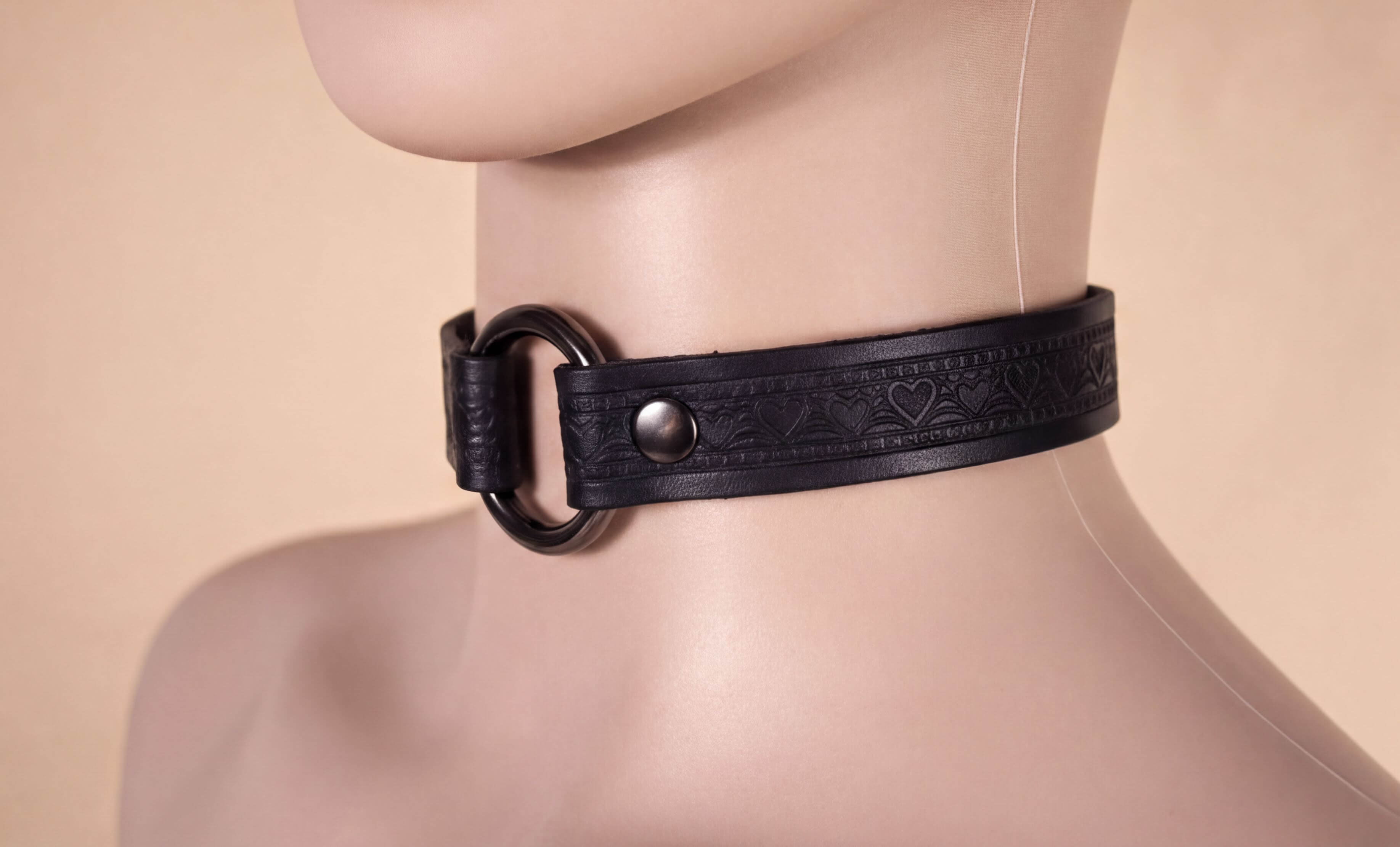 A close-up view of a mannequin head wearing a black leather choker necklace with a circular metal ring.