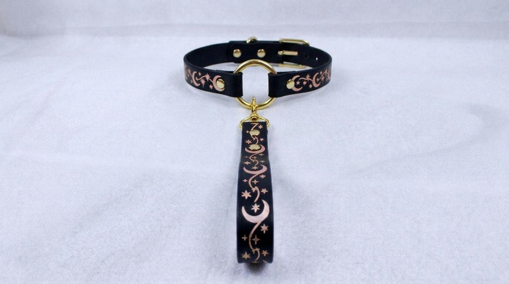 A black collar with a gold-colored buckle and a decorative strap featuring a moon and star pattern.