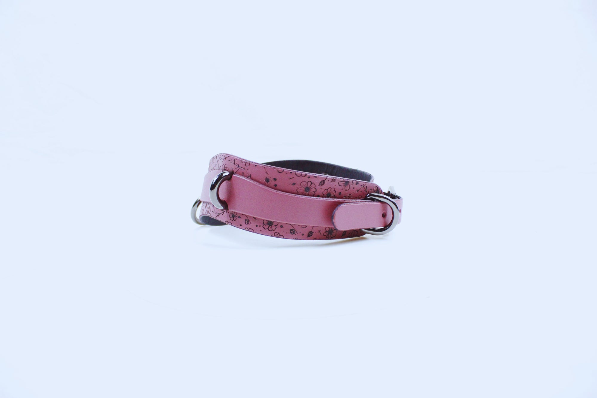 A pink leather collar with a floral pattern and metal buckle is shown against a white background.