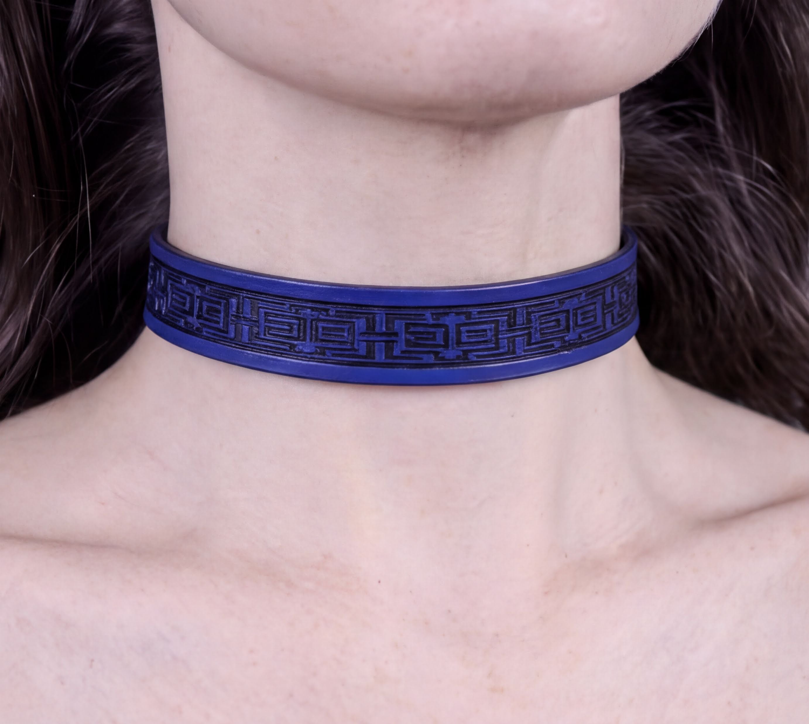 A close-up view of a person's neck and chest area wearing a blue choker necklace with a black geometric pattern.