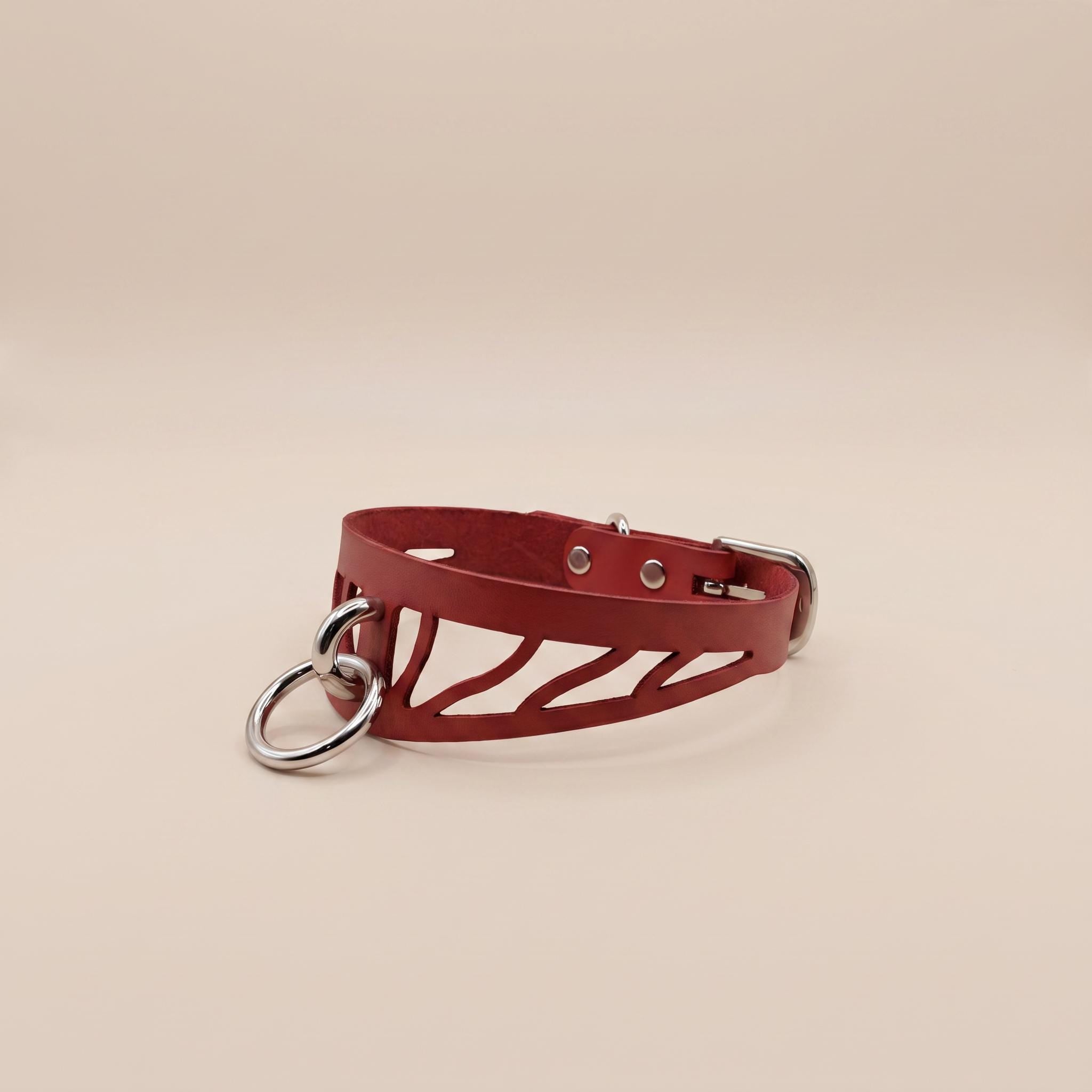 A red leather choker necklace with metal rings and a metal clasp is shown against a light background.