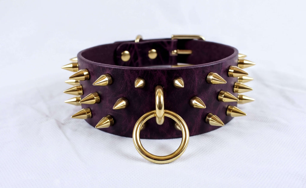 A purple leather choker necklace with gold spikes and a gold ring is displayed against a white background.