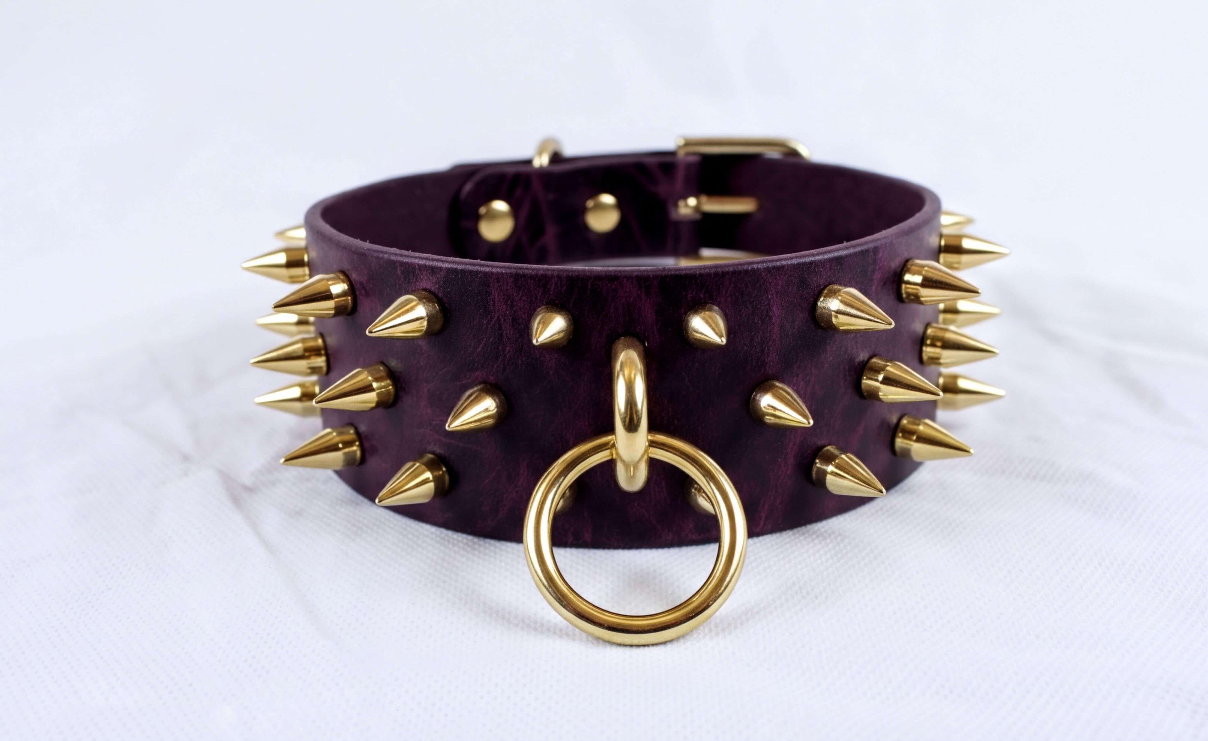 A purple leather choker necklace with gold spikes and a gold ring is displayed against a white background.