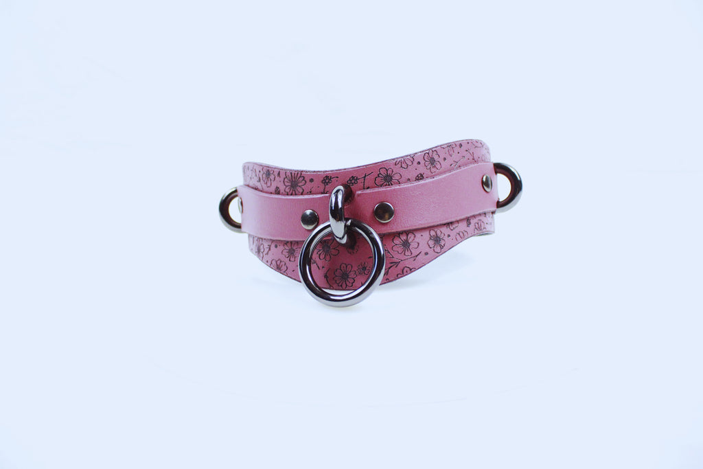 A pink leather choker necklace with a floral pattern and metal rings.