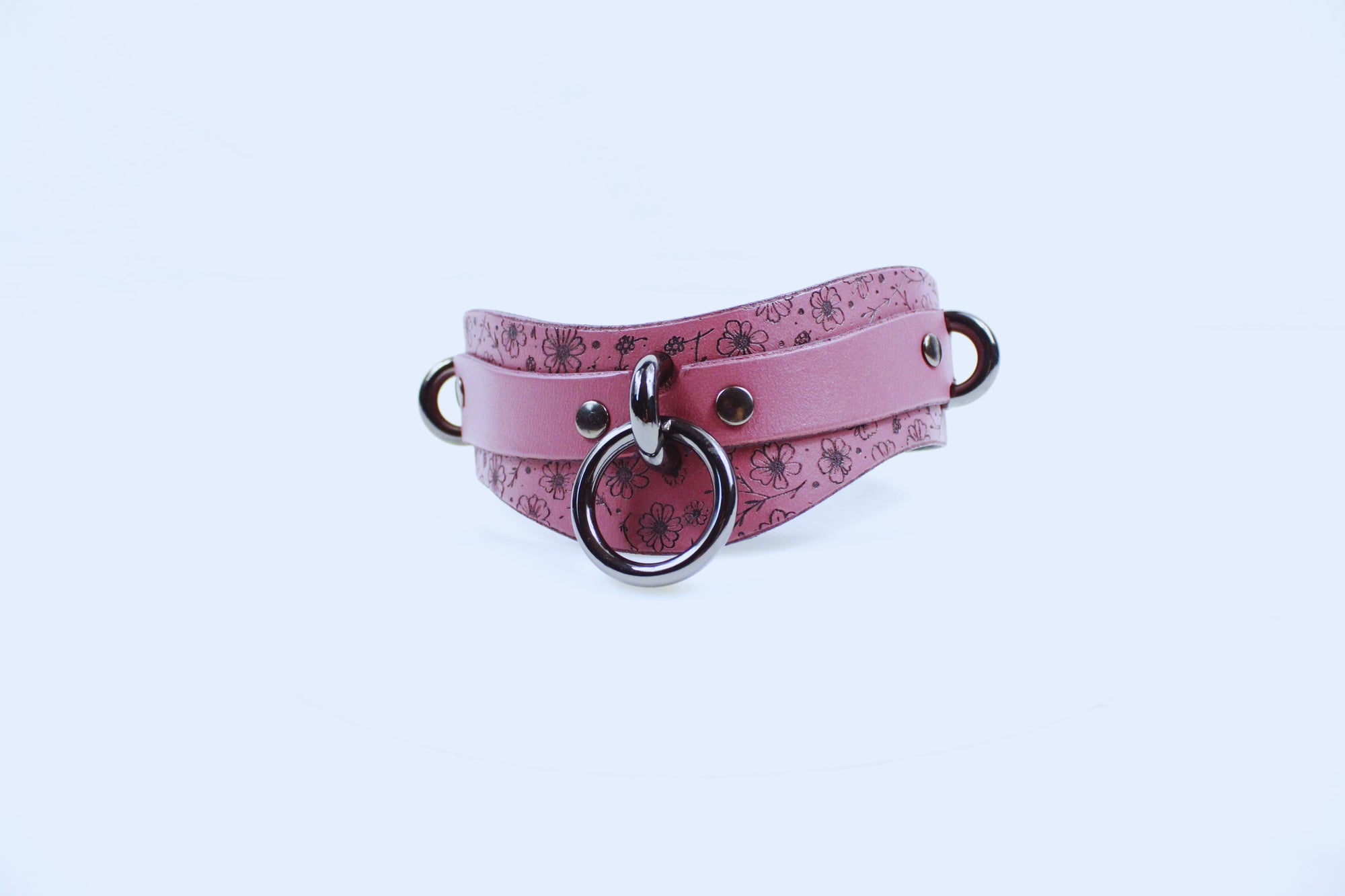 A pink leather choker necklace with a floral pattern and metal rings.