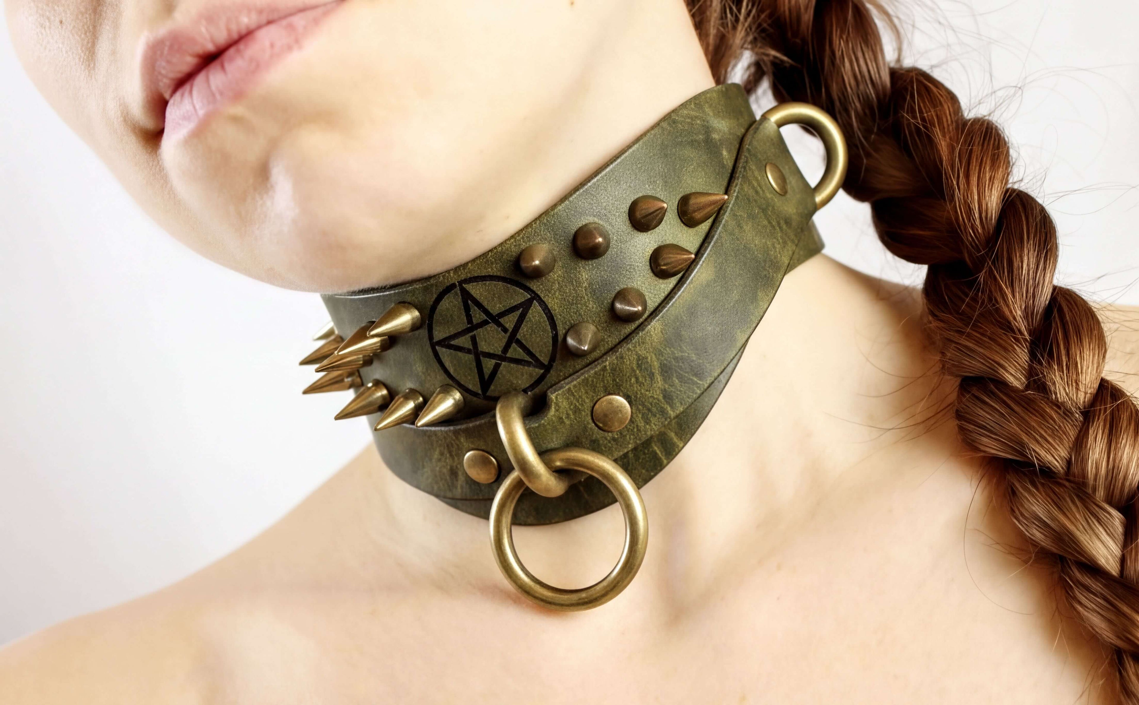 A close-up of a woman's neck wearing a green leather choker necklace with spikes and a pentagram symbol.
