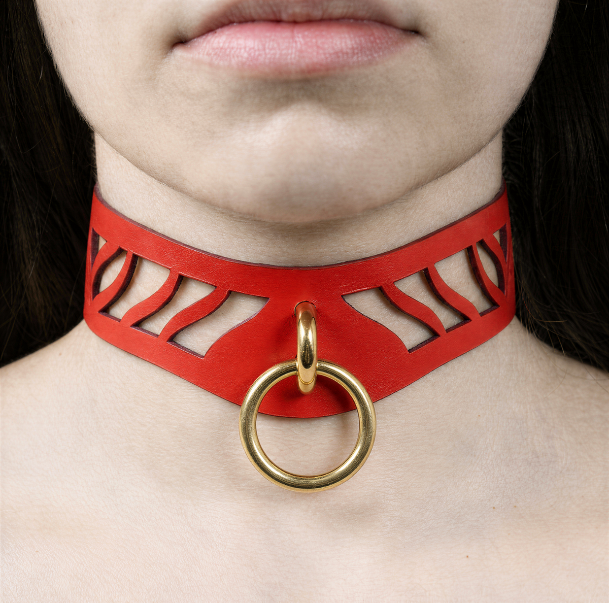 A close-up of a person's neck and chest area wearing a red choker necklace with a gold ring.
