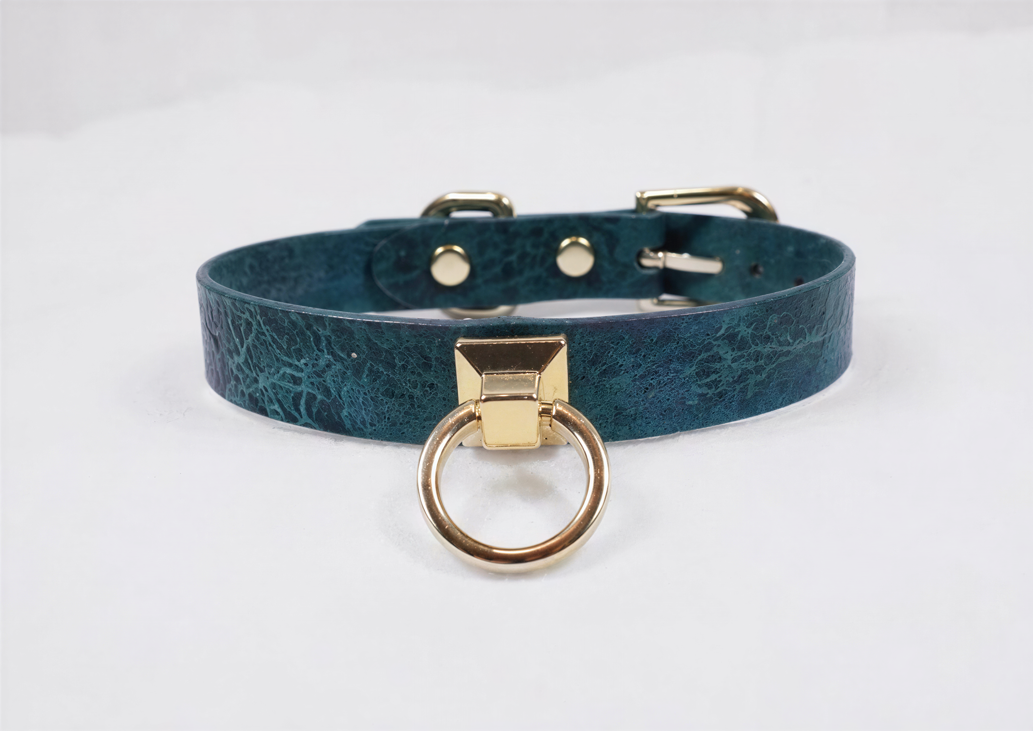 A teal-colored leather choker collar with a gold-colored metal ring and buckle.