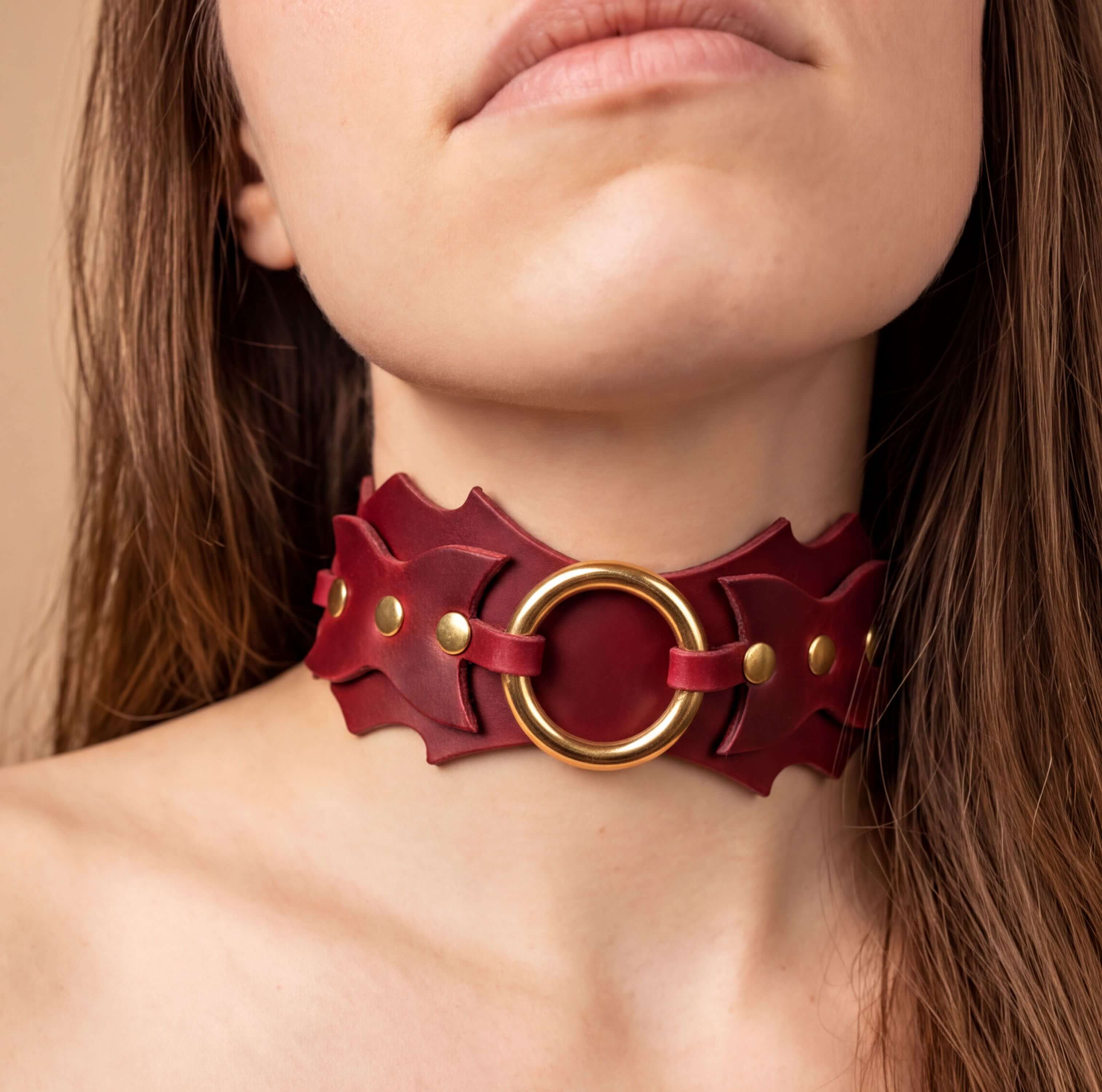 A close-up of a woman's neck wearing a red leather choker necklace with a gold ring.