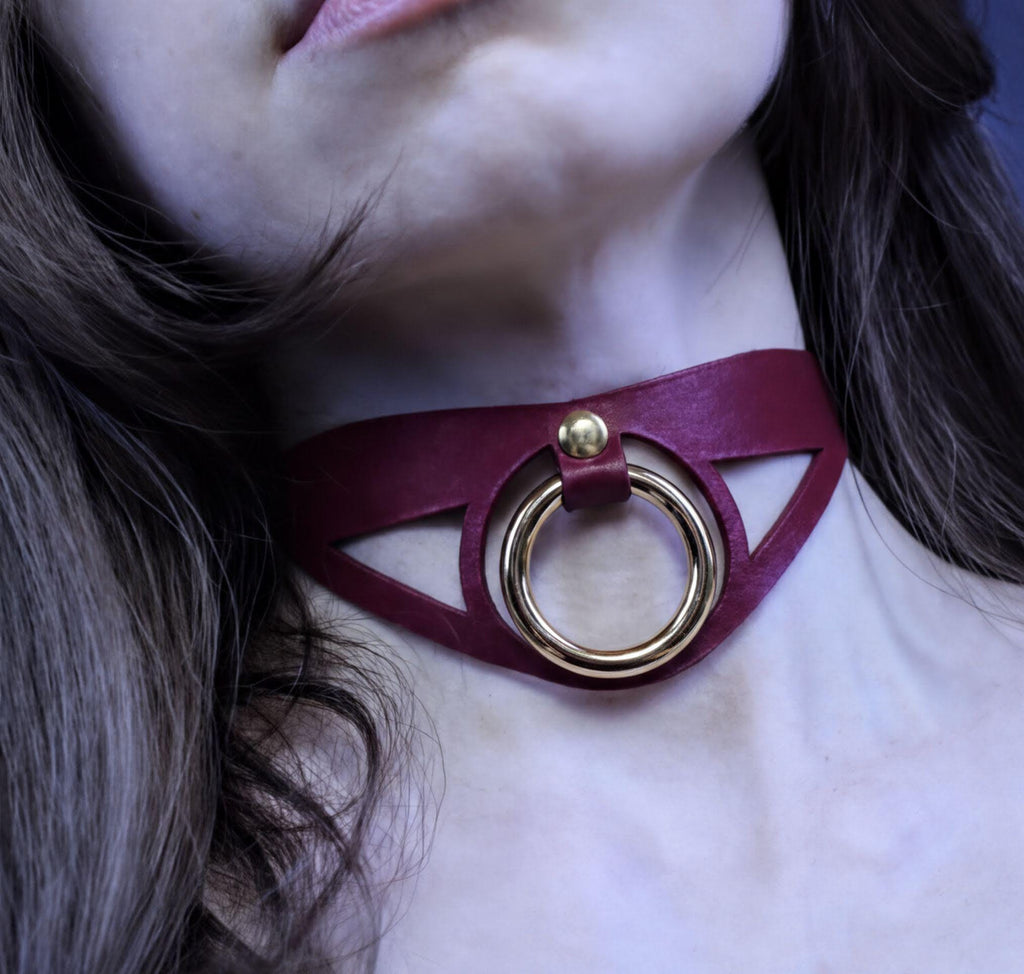 A close-up of a woman's neck with a burgundy choker necklace featuring a gold ring.