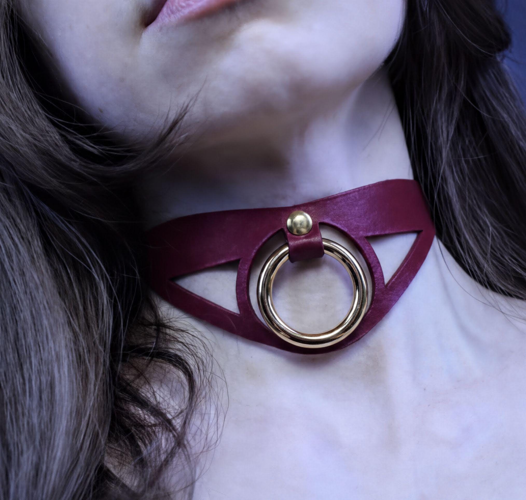A close-up of a woman's neck with a burgundy choker necklace featuring a gold ring.