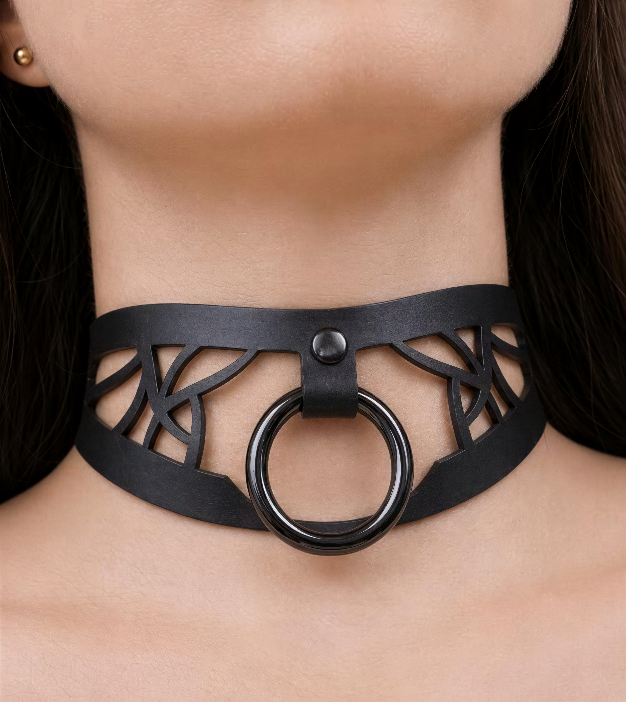 A close-up of a woman's neck wearing a black choker necklace with a circular ring on the front.
